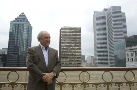 David Azrieli debout devant trois gratte-ciel.