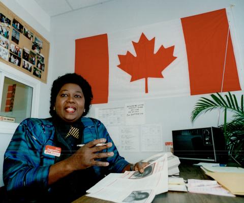 Jean Augustine, assise à un bureau devant un drapeau canadien.