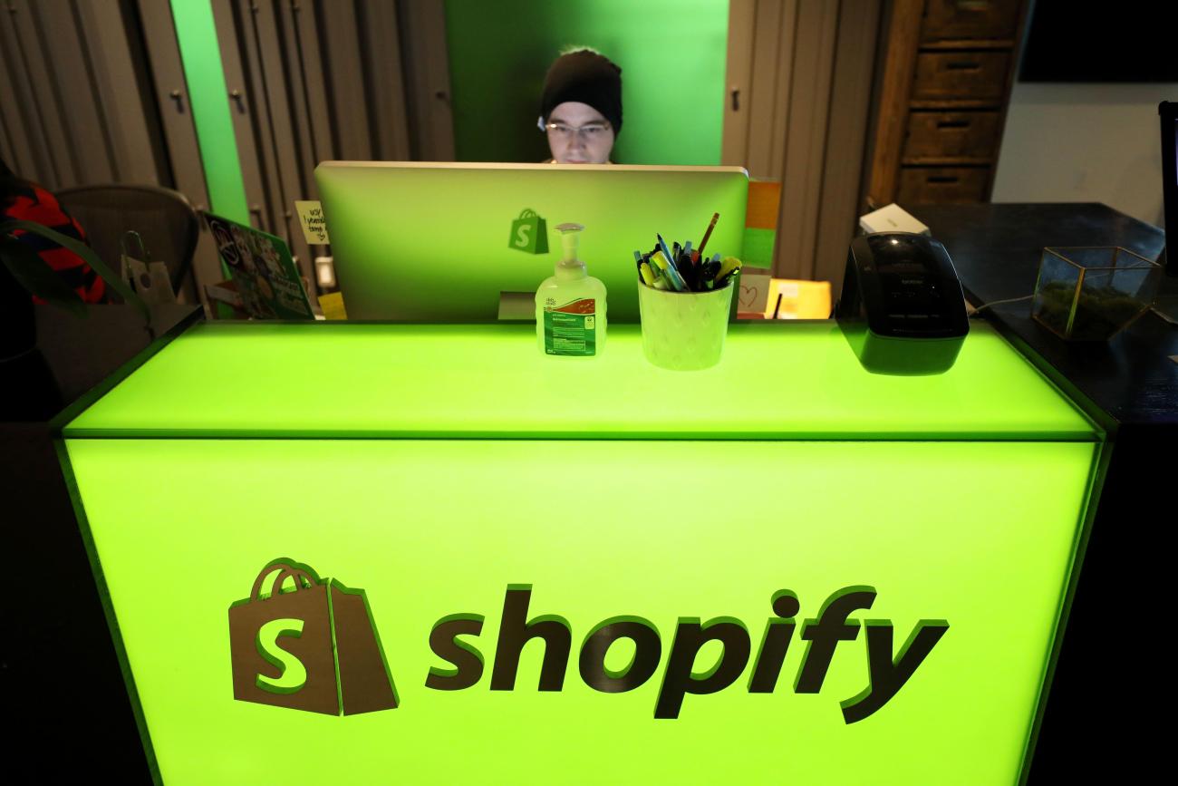 Homme regardant un écran derrière un bureau rétroéclairé vert avec le logo Shopify.