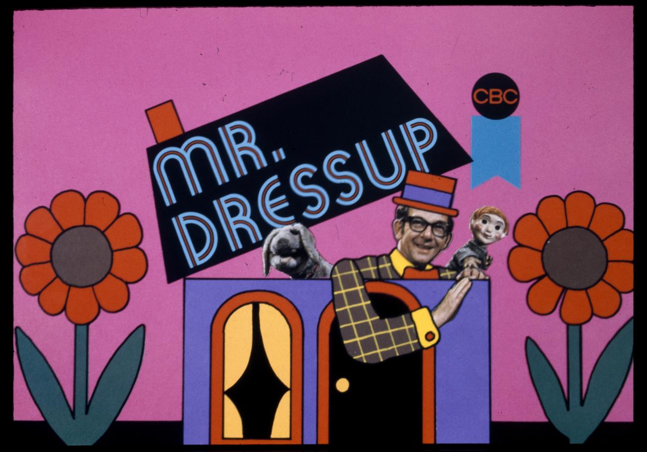 Graphique coloré d’une maison et de fleurs avec Ernie Coombs et deux marionnettes de Mr. Dressup.