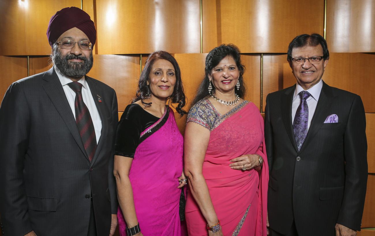Photo de Steve Gupta en costume avec trois personnes, dont deux femmes en saris et un homme en costume portant un turban.
