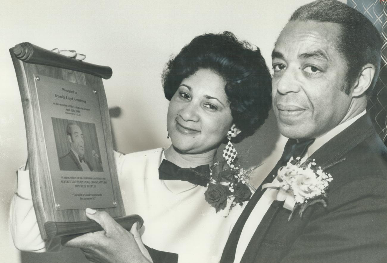 Bromley Armstrong et une femme tenant une plaque sur laquelle figurent un texte et une photo de Bromley Armstrong.