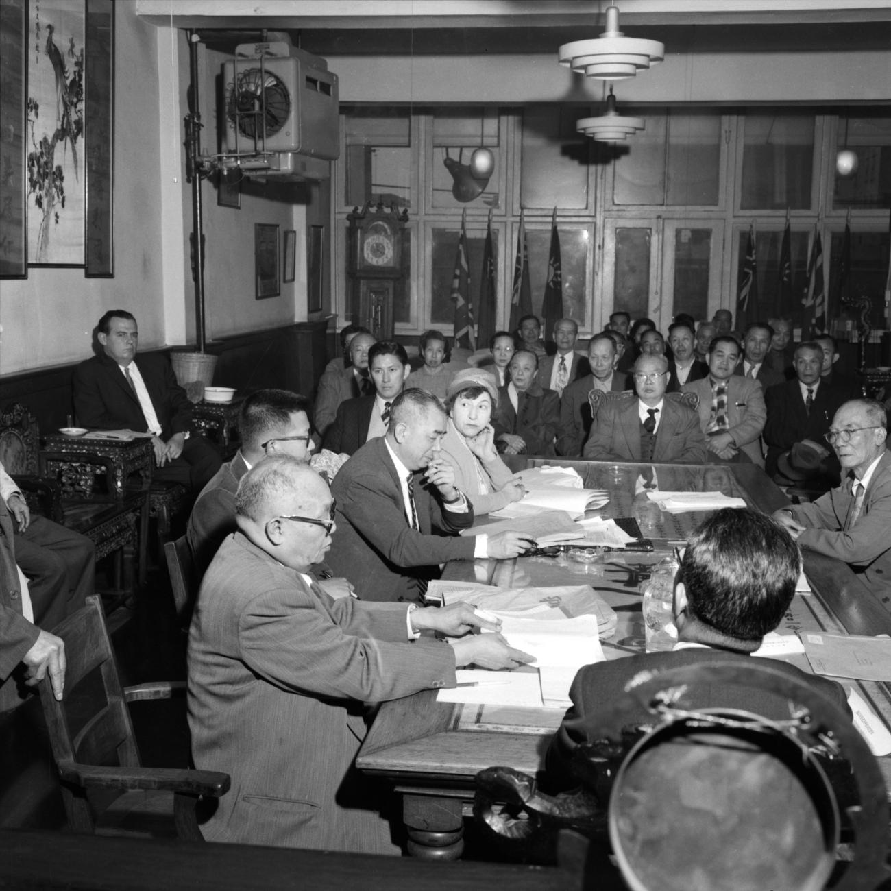 Wong Foon Sien assis à une table avec cinq autres personnes et d’autres gens assis dans les autres rangées de chaises.