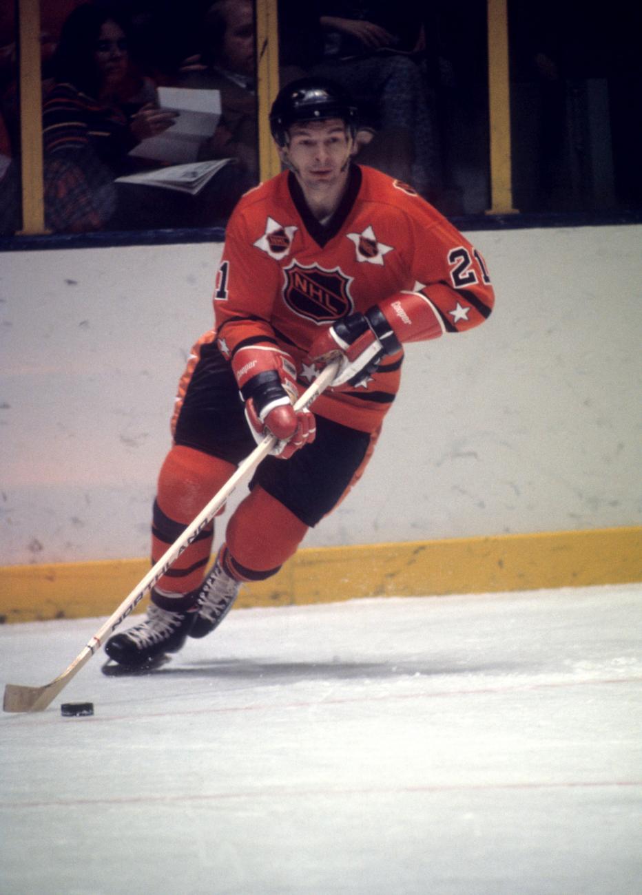 Stan Mikita, en uniforme rouge, patine en tenant un bâton de hockey.