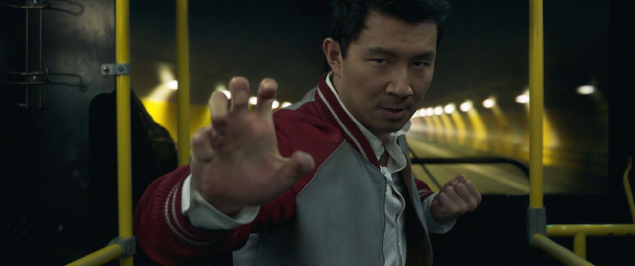 Simu Liu, dans le rôle de Shang-Chi, lève sa main droite, les doigts écartés, comme s’il se préparait à un combat.