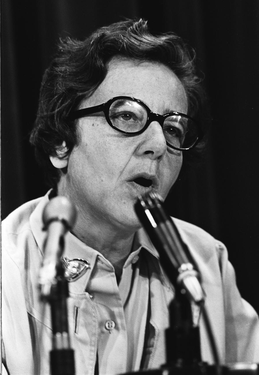 Une femme parle dans des microphones placés sur la table devant elle.